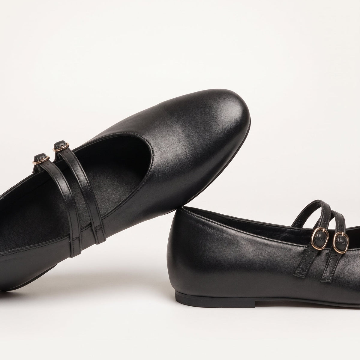 Close-up of a pair of Rebecca Allen The Capital Flat double-strap Mary Jane flats in Black leather, one resting on the other
